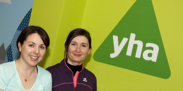 Two women standing in front of the YHA logo